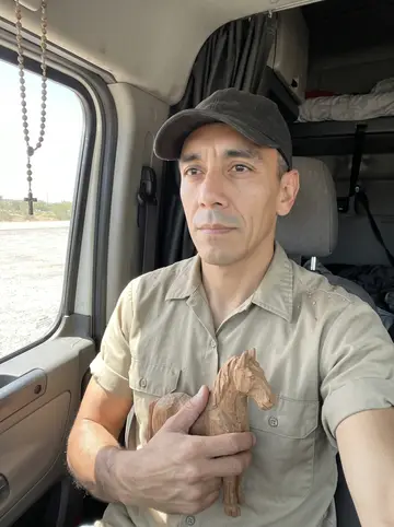Lalo, AI character: the back edge of the flatbed parked at a quiet roadside rest area at sunset, pale wood shavings on the…