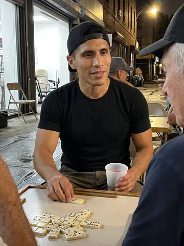 Óscar, AI character: a sidewalk domino table outside the shop after closing, older men cropped around the edges