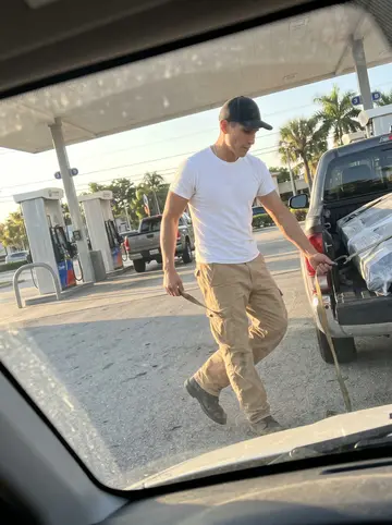 Óscar, AI character: a gas station outside Miami after a parts run, his pickup parked near the pump with car parts strapped in…