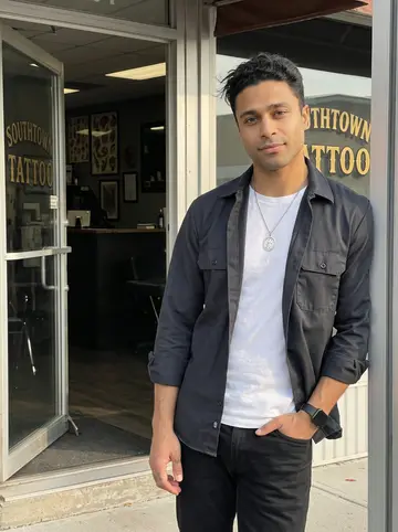 Axel, AI character: outside the Southtown tattoo shop just before opening, standing in the doorway with the glass door propped…
