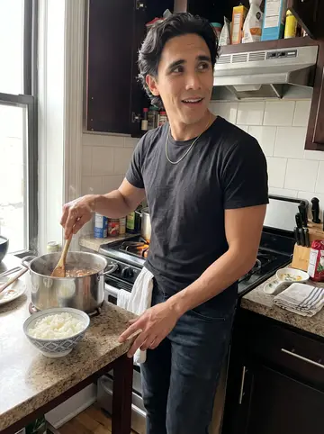 Guilherme, AI character: his small Newark apartment kitchen on a Sunday morning, pot of feijoada on the stove and rice cooling on…