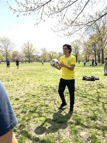 Guilherme, AI character: a small Newark park on a bright spring Sunday, neighbors playing casual football on worn grass