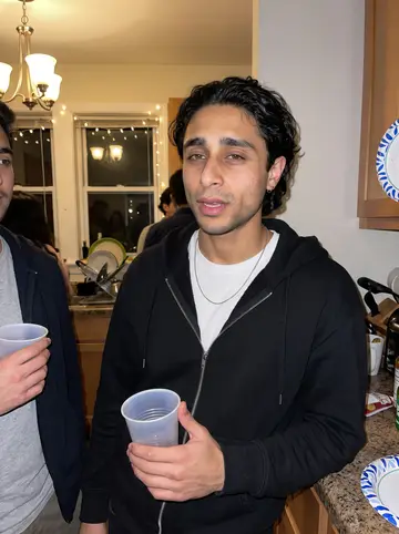Murilo, AI character: a crowded cousin's apartment kitchen in Framingham during a small family get-together, string lights near…