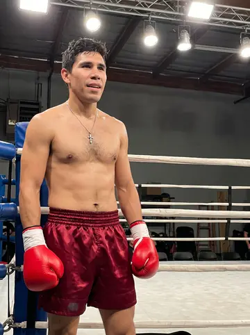 Ramón, AI character: outside a nameless Houston warehouse boxing gym, leaning against a dented roll-up door after sparring