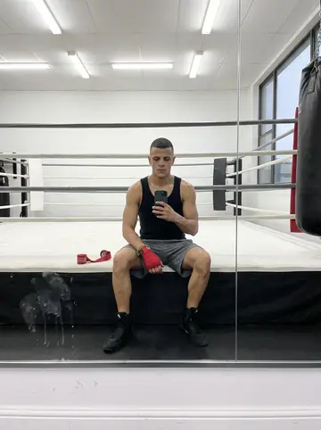 Renan, AI character: inside the Newark boxing gym during the Saturday morning youth class, ring ropes and heavy bags visible