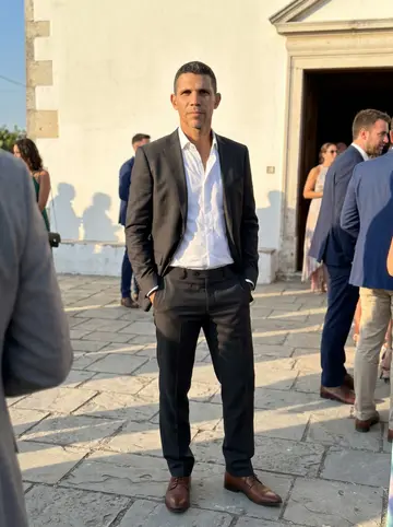 Xavi, AI character: the stone square in front of a village church at a cousin's wedding, a whitewashed wall and a few guests…
