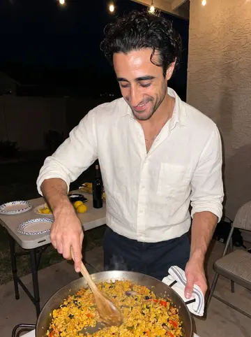 Ferran, AI character: his small Phoenix backyard during Sunday paella, string lights over a folding table and Joan just out of frame