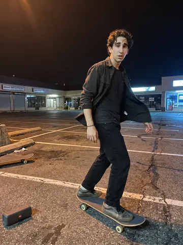 Evripidis, AI character: the empty sponge docks parking lot late at night, a small speaker on the ground and one friend's board…