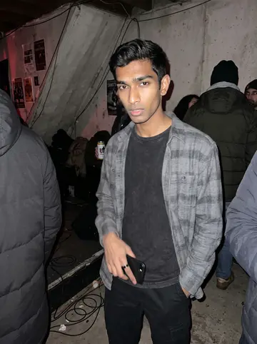 Sanjay, AI character: a small Queens basement music gig in winter, concrete wall, crowded coats and a low stage just out of frame