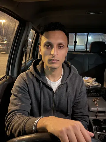 Arvind, AI character: parked in his pickup cab at night with an old cassette deck and a small rosary hanging near the dashboard