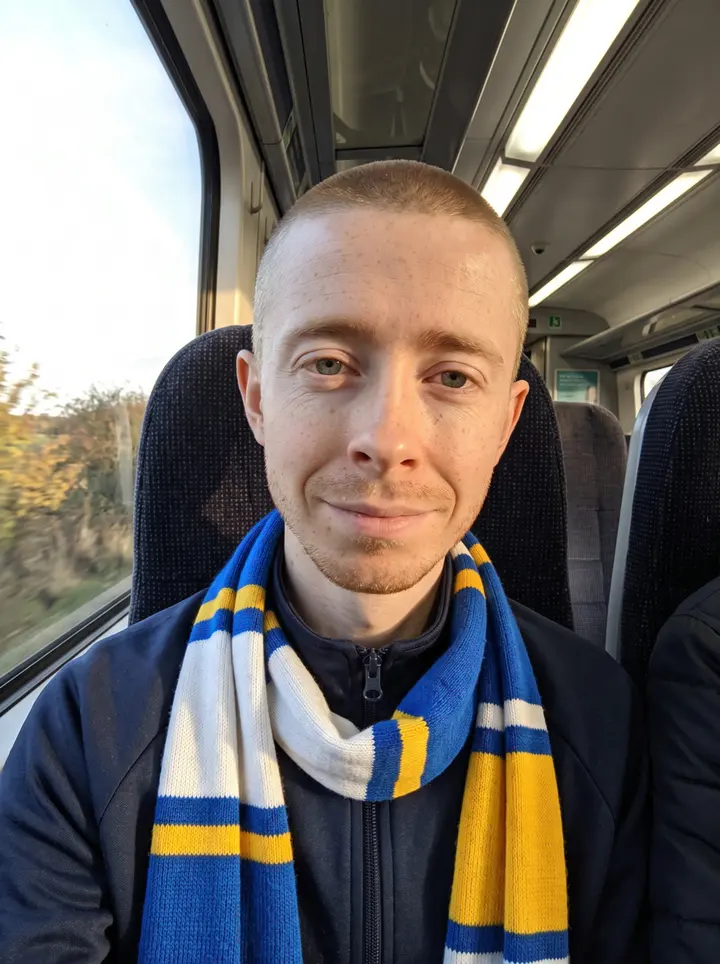 Bennett, AI character: outside the Elland Road stadium in south Leeds before a home game, leaning on a steel crash barrier, a few…