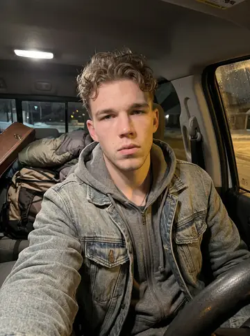 Reece, AI character: inside his parked Ford Ranger on a cold winter night, dome light on, sleeping bag and a backpack visible…
