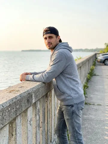 Christian, AI character: a quiet Lake Erie overlook on a Sunday evening, water and low concrete railing behind him