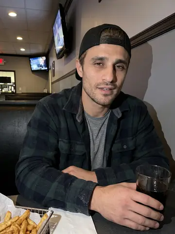 Christian, AI character: a small Youngstown corner bar after work, near a high table with a basket of fries and a garage ball game…