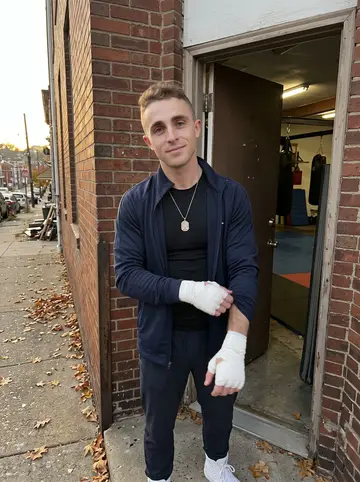 Samuel, AI character: outside a small Pittsburgh boxing gym in late autumn, brick wall and open gym door behind him
