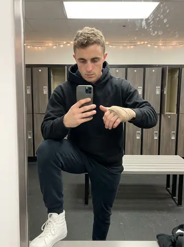 Samuel, AI character: boxing gym locker room mirror in December, holiday string lights reflected faintly near the ceiling