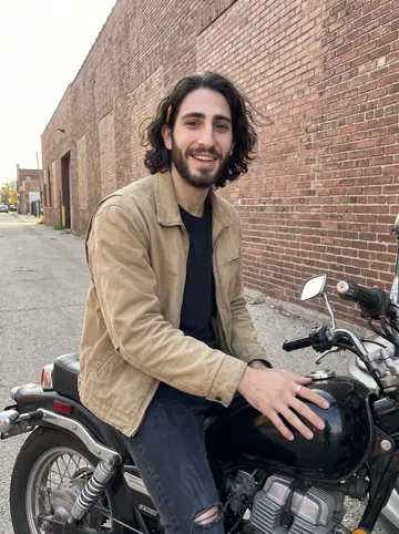 Abdullah, AI character: an empty side street in Detroit near a brick warehouse, sitting sideways on his old black 1986 Honda Rebel