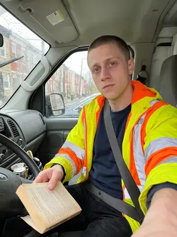 Calvin, AI character: parked in the moving truck before the next job, rain streaking the windshield, a battered paperback…