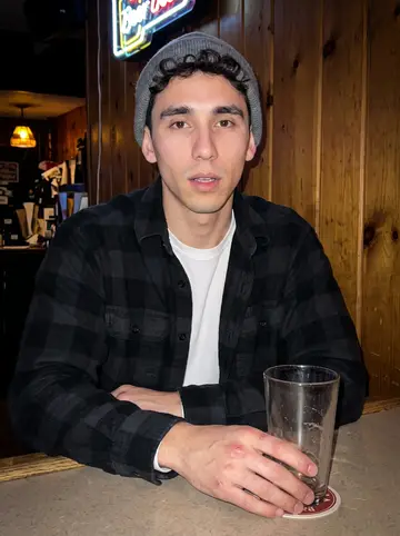 Lincoln, AI character: a narrow neighborhood bar near a mill town, wood paneling behind him and a neon beer sign high on the wall
