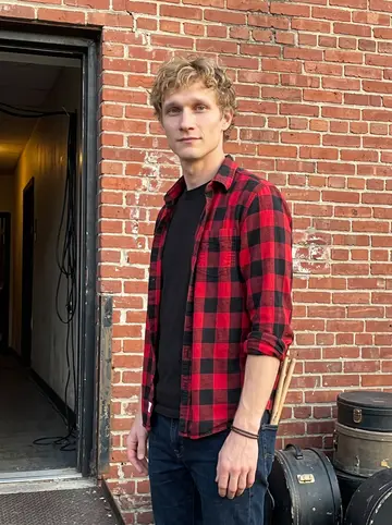 Cory, AI character: outside the back door of a small Dayton punk venue after soundcheck, brick wall, loading ramp, and drum…