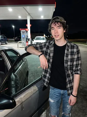 Blake, AI character: gas station lot off an Austin frontage road after a late delivery route, his taped-up Honda Civic beside him