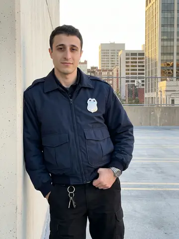 Neil, AI character: top level of a downtown Baltimore parking garage just before his night shift, concrete wall and city…