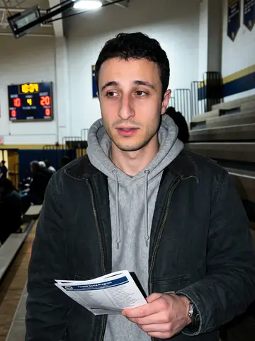 Neil, AI character: top row of a Baltimore high school gym during his nephew's basketball game, bleachers and scoreboard glow…