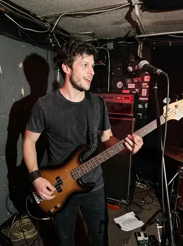 Damian, AI character: a cramped Tulsa dive bar stage during his garage band's unpaid late-night set