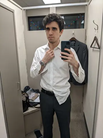 Curtis, AI character: a small suit-rental fitting room in Seattle with winter holiday lights reflected faintly outside the shop…