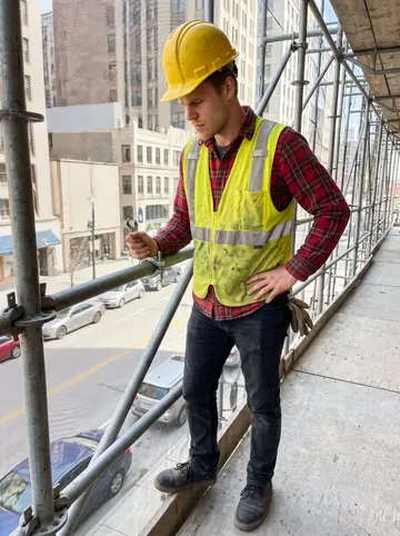 Tyson, AI character: a scaffold lift on a downtown renovation site, Detroit street traffic visible below through the frame