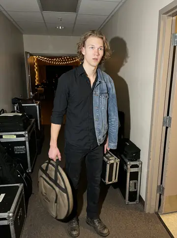 Leevi, AI character: the back hallway of a Duluth wedding hall during a Saturday load-in, cases stacked near a service door and…