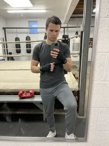 Eugene, AI character: inside the old boxing gym during the Tuesday kids class, worn canvas ring and heavy bags behind him