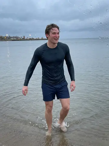 Gijs, AI character: Lake Michigan shoreline in October after a dare swim, grey water and wet sand behind him near Holland…
