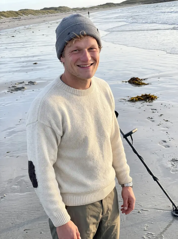 Tor, AI character: a wide sandy beach near Sola at low tide, wet sand shining, he leans on the long pole of his metal…
