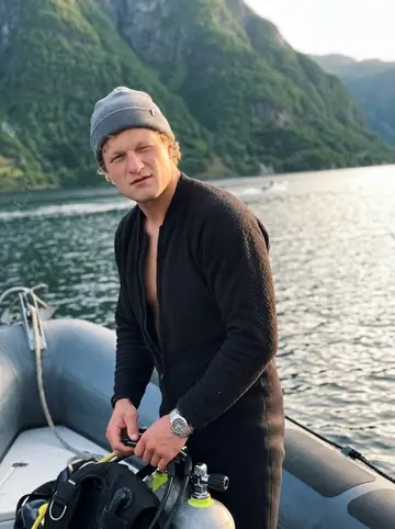 Tor, AI character: the bow of a small RIB dive boat in a Ryfylke fjord, tanks and a dive bag at his feet, steep green…