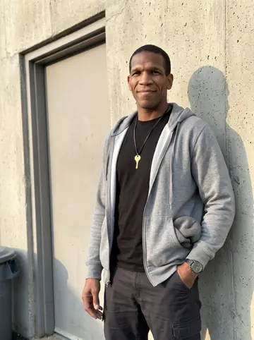 Kerry, AI character: outside the Cleveland warehouse after shift, leaning against a plain concrete wall near the employee door