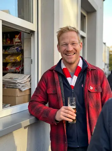 Henrik, AI character: on the street corner outside his Büdchen kiosk in Cologne's Südstadt, leaning an elbow on the open sales…