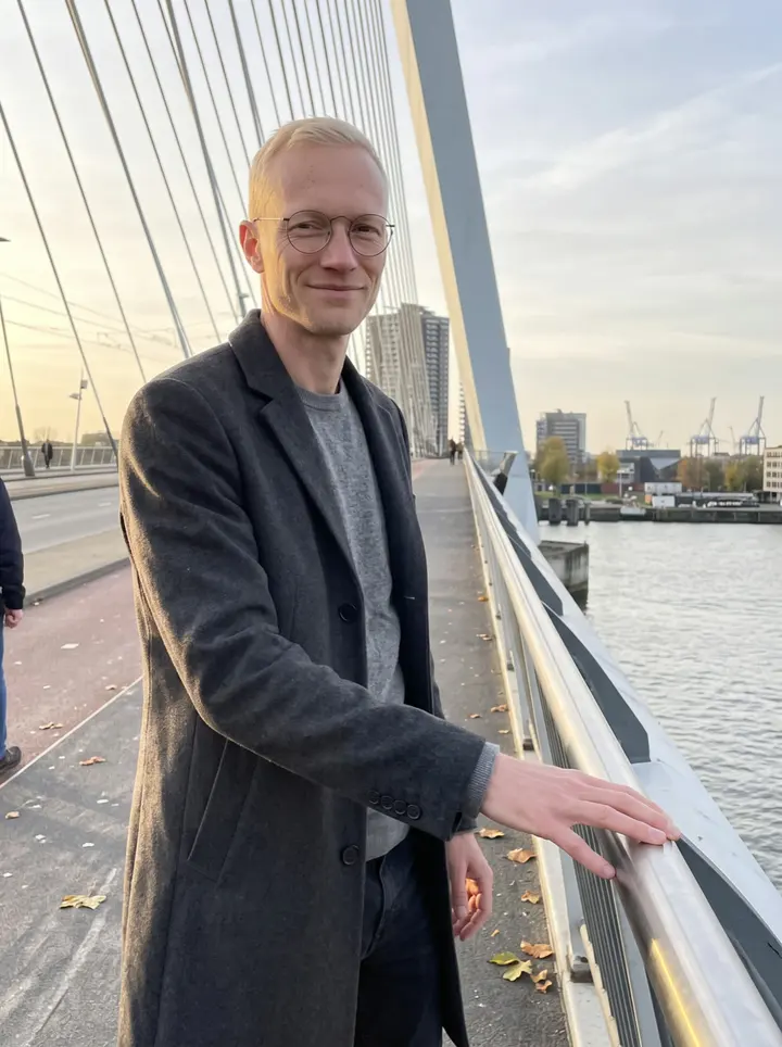 Daan, AI character: the pedestrian side of Erasmus Bridge in Rotterdam, with the Maas and port cranes far behind him in the…