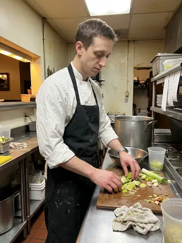 Dale, AI character: the prep station of a small Scranton restaurant near closing time, stainless counter, stock pots and a…