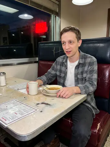 Dale, AI character: a worn diner booth in Scranton before nine, laminated menu, coffee mug and a bowl of soup on the table