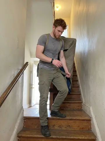 Euan, AI character: inside a Philadelphia rowhouse stairwell during a piano move, narrow painted walls and worn wooden steps