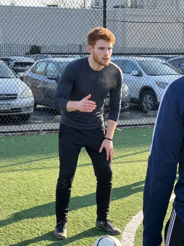 Euan, AI character: a fenced five-a-side football pitch in South Philadelphia on a cold Sunday morning, chain-link fence and…