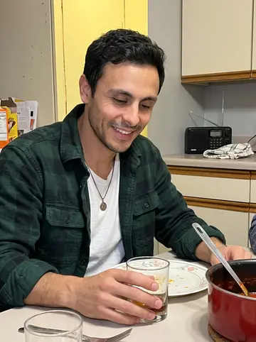 Eliseo, AI character: his aunt's kitchen in South Philly on a Sunday night, red sauce pot on the table, Phillies radio on the…