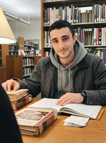 Brando, AI character: a quiet table in the Providence Public Library cookbook section, a stack of worn cookbooks beside his elbow