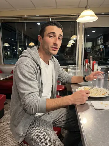 Brando, AI character: a late-night diner counter in Providence after closing shift, red vinyl stools and a half-finished plate…