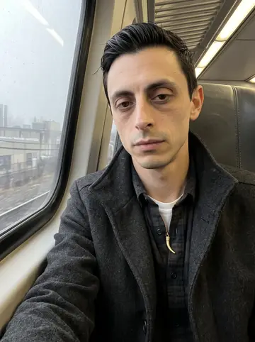 Onofrio, AI character: a foggy morning NJ Transit train into Newark, window glass reflecting pale grey light and blurred…