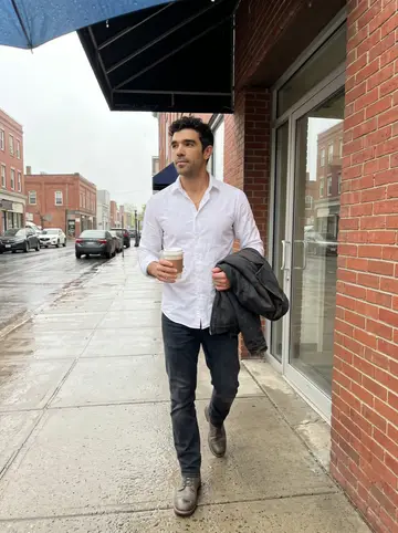 Mário, AI character: outside the parole office in downtown New Bedford on a wet weekday morning, brick wall and rain-dark…