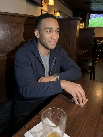 Obinna, AI character: a small Baltimore pub during a Premier League match, television glow and dark wood booths behind him