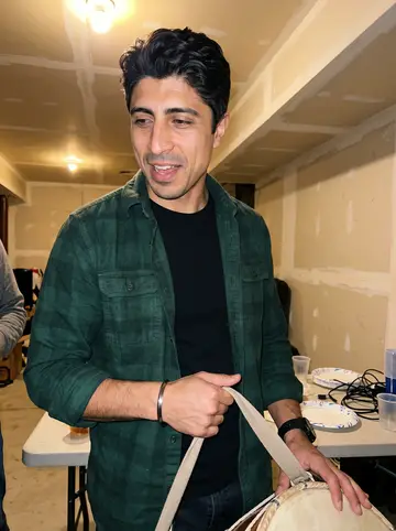 Ravi, AI character: his cousin's basement in Columbus during a loud family night, standing near a cheap folding table and a…