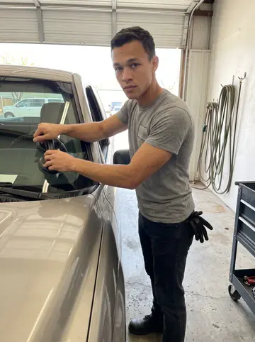 Hunter, AI character: the open bay of a small auto glass shop in Tulsa, a pickup truck pulled halfway inside